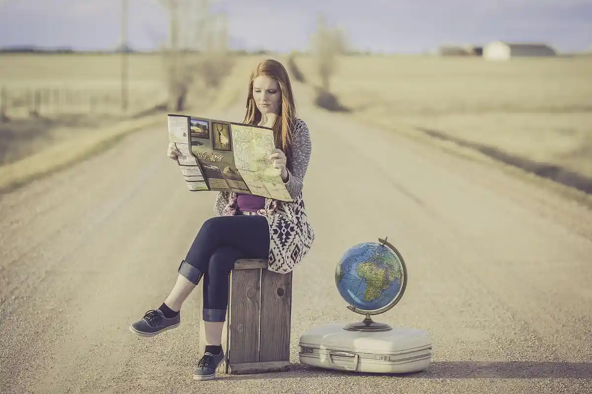 Woman sitting on a road with a map, globe, and suitcase planning her travel route